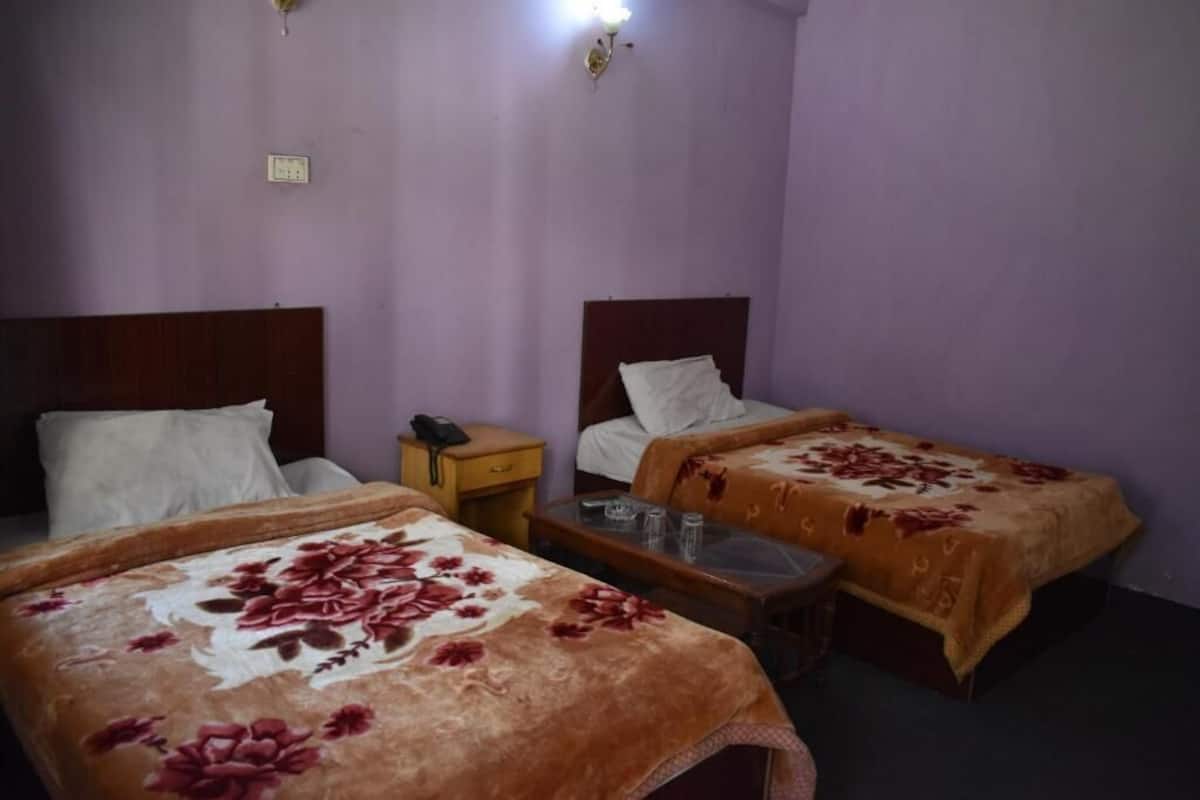 A room with two beds, each with a wooden headboard and a floral bedspread. There is a small wooden nightstand with a lamp and a telephone.