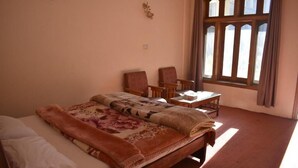 Une pièce comprenant un lit, deux chaises, une petite table et une fenêtre avec des rideaux.
