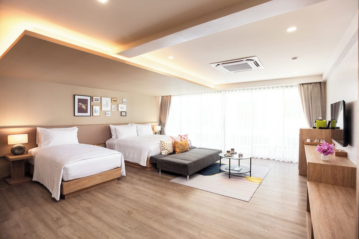 A modern hotel room with two beds, a sofa, a small table, and a TV.
