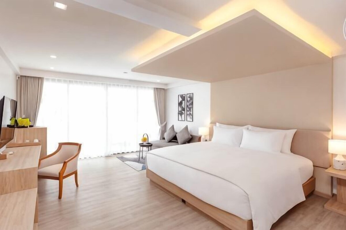 A hotel room with a large bed, a desk, a chair, a TV, and a window with curtains.