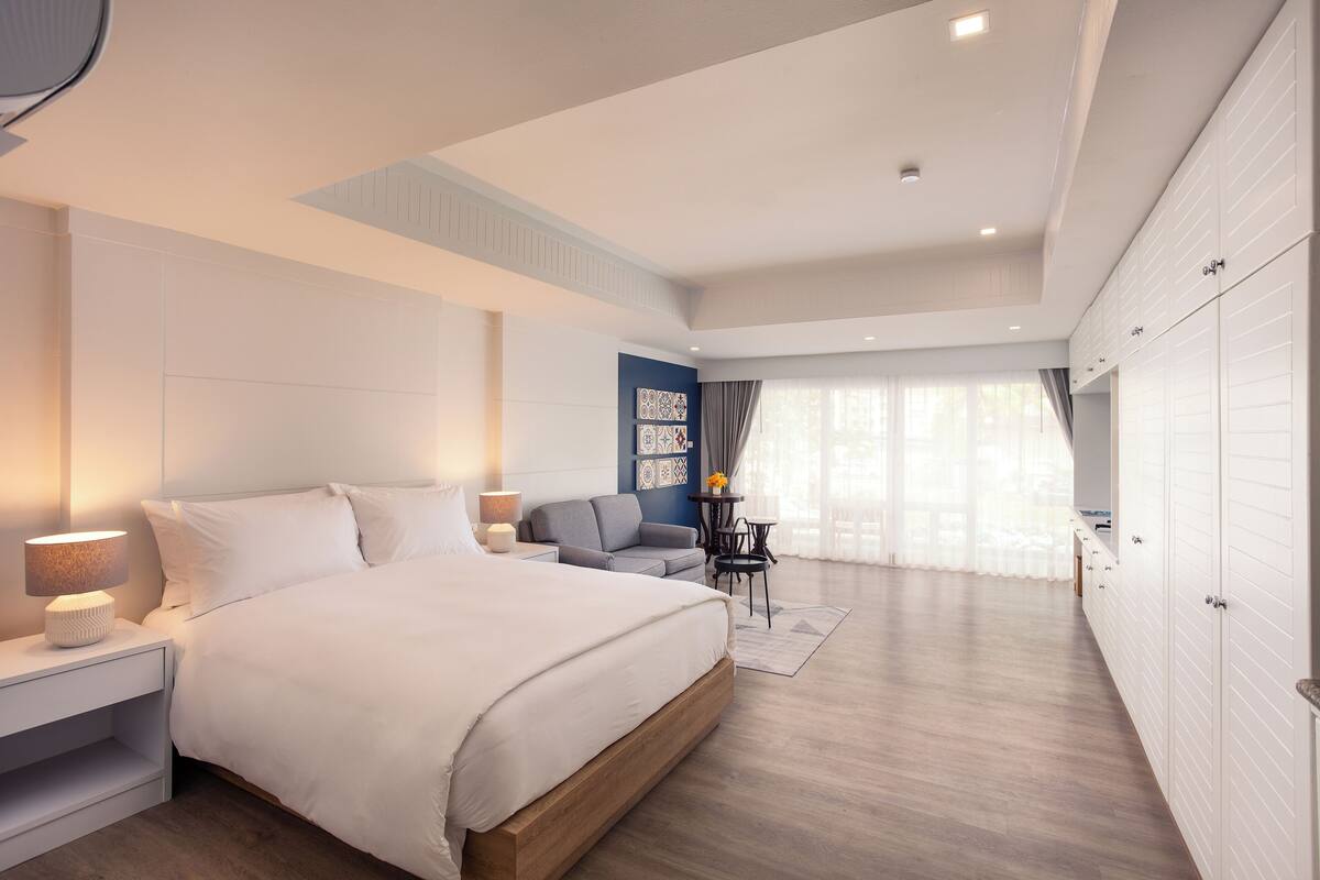 A modern bedroom with a large bed, bedside tables, a seating area with a sofa, and a wardrobe.