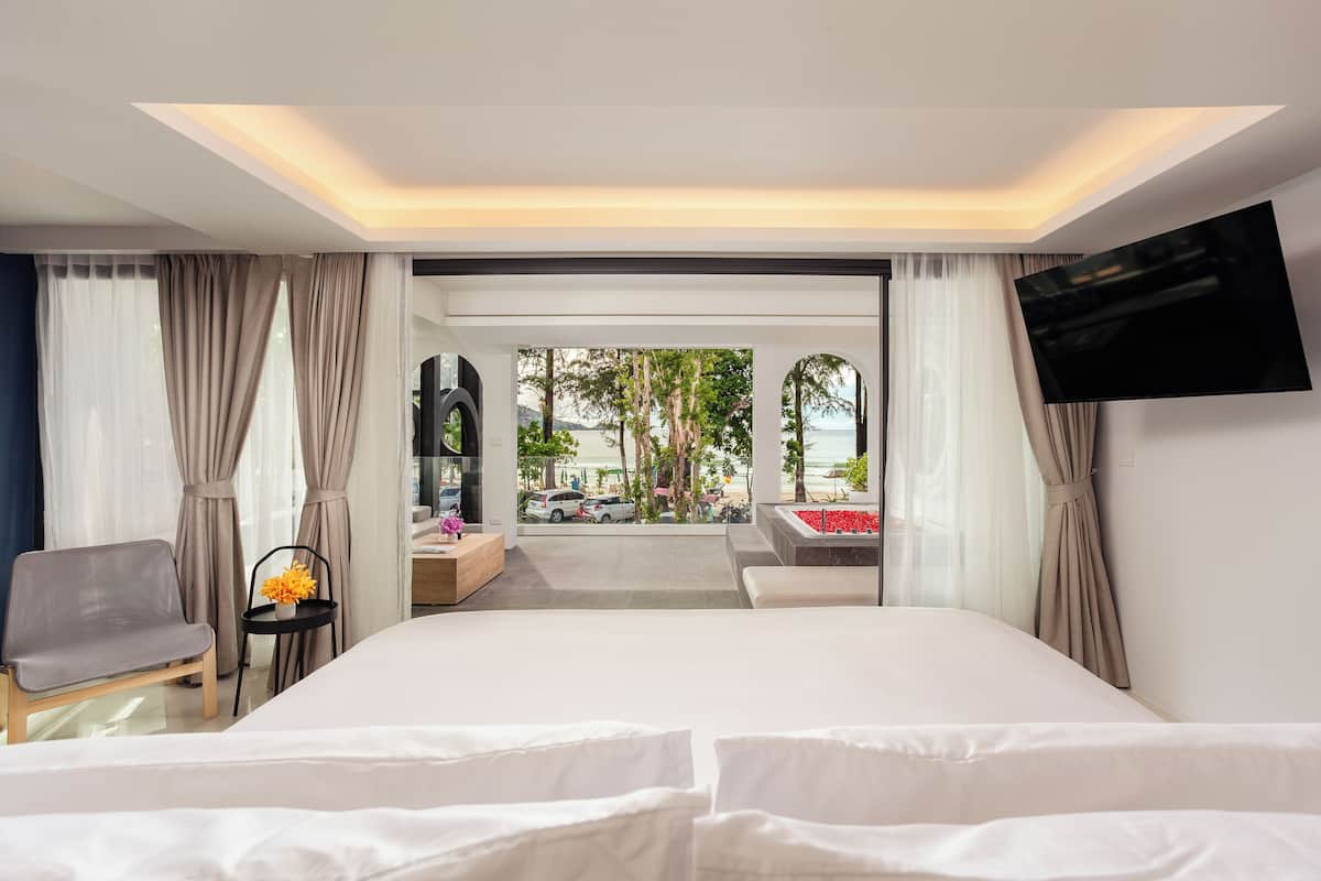 A hotel room with a bed, a TV, a desk, and a view of the beach.