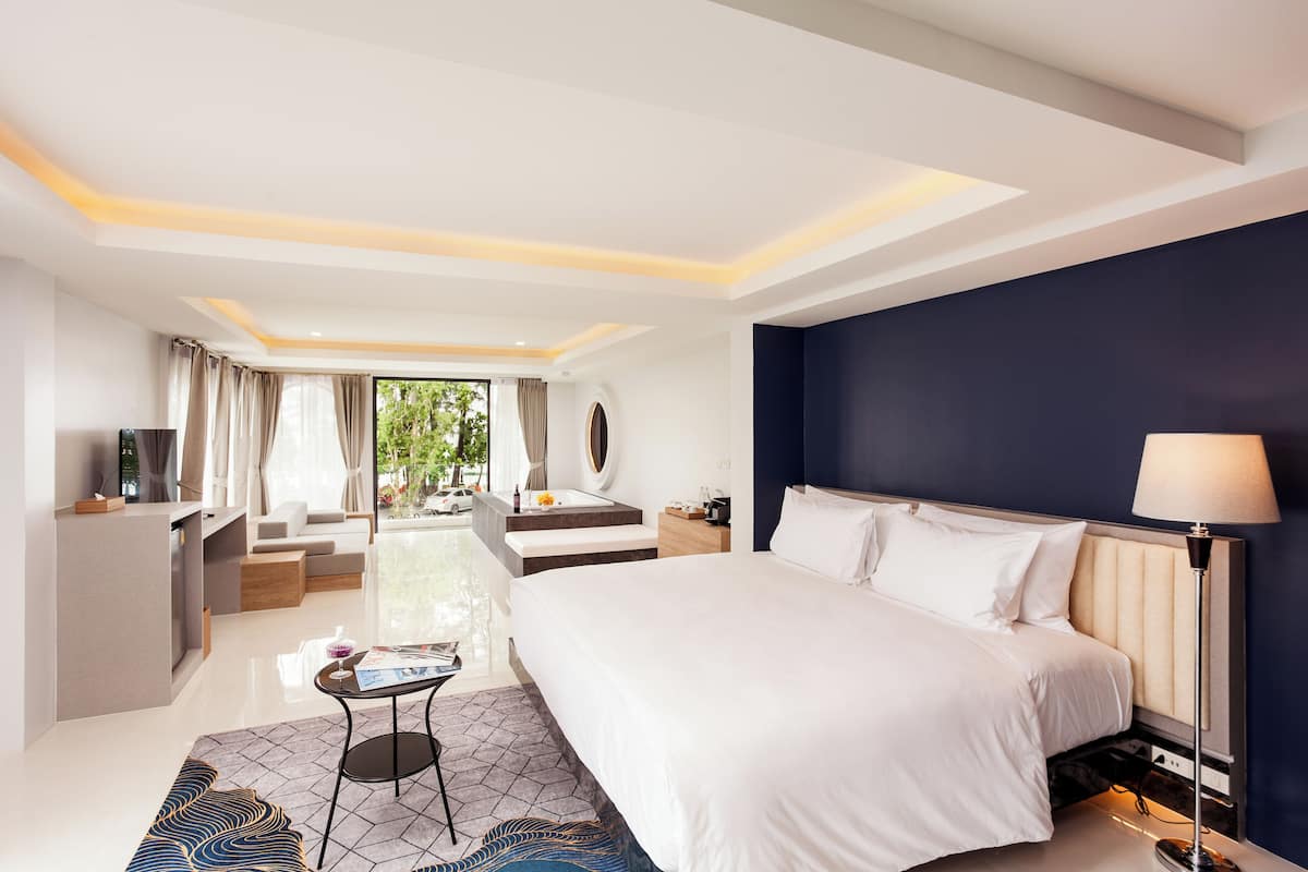 A modern hotel room with a large bed, a desk, a sofa, and a view of the outdoors.