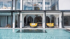 Un hotel moderno con piscina, zona de sofás con dos opciones amarillas y un salón con paredes de vidrio.
