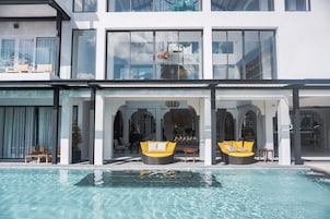 Un hotel moderno con piscina, zona de sofás con dos opciones amarillas y un salón con paredes de vidrio.