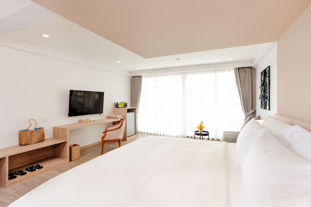 A modern hotel room with a large bed, a desk with a chair, a TV, and a window with curtains.