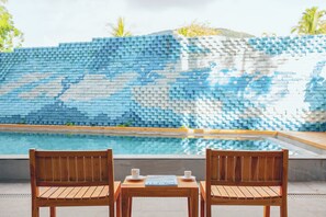 Una zona junto a la piscina con un banco y mesa de madera, una pared de azulejos con diseño azul y blanco, y vista despejada a la piscina.