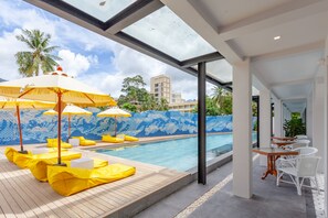 Zona de piscina con sillas de descanso amarillas y sombrillas, pared de azulejos con mosaico azul y vista despejada de la piscina.