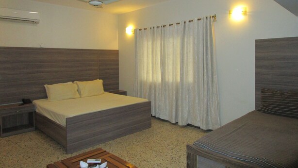Quarto com cama, mesa de cabeceira, mesa de centro de madeira, ventoinha no teto e janela com cortinas.