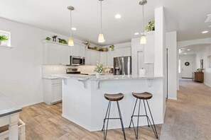 A modern kitchen with white cabinetry, stainless steel appliances, and a central island with stools.