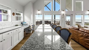 A spacious kitchen with a long island, white cabinetry, and a view to the outside. - Beachfront | Pool | Ocean Views, Loft & Bar (Gilchrist)