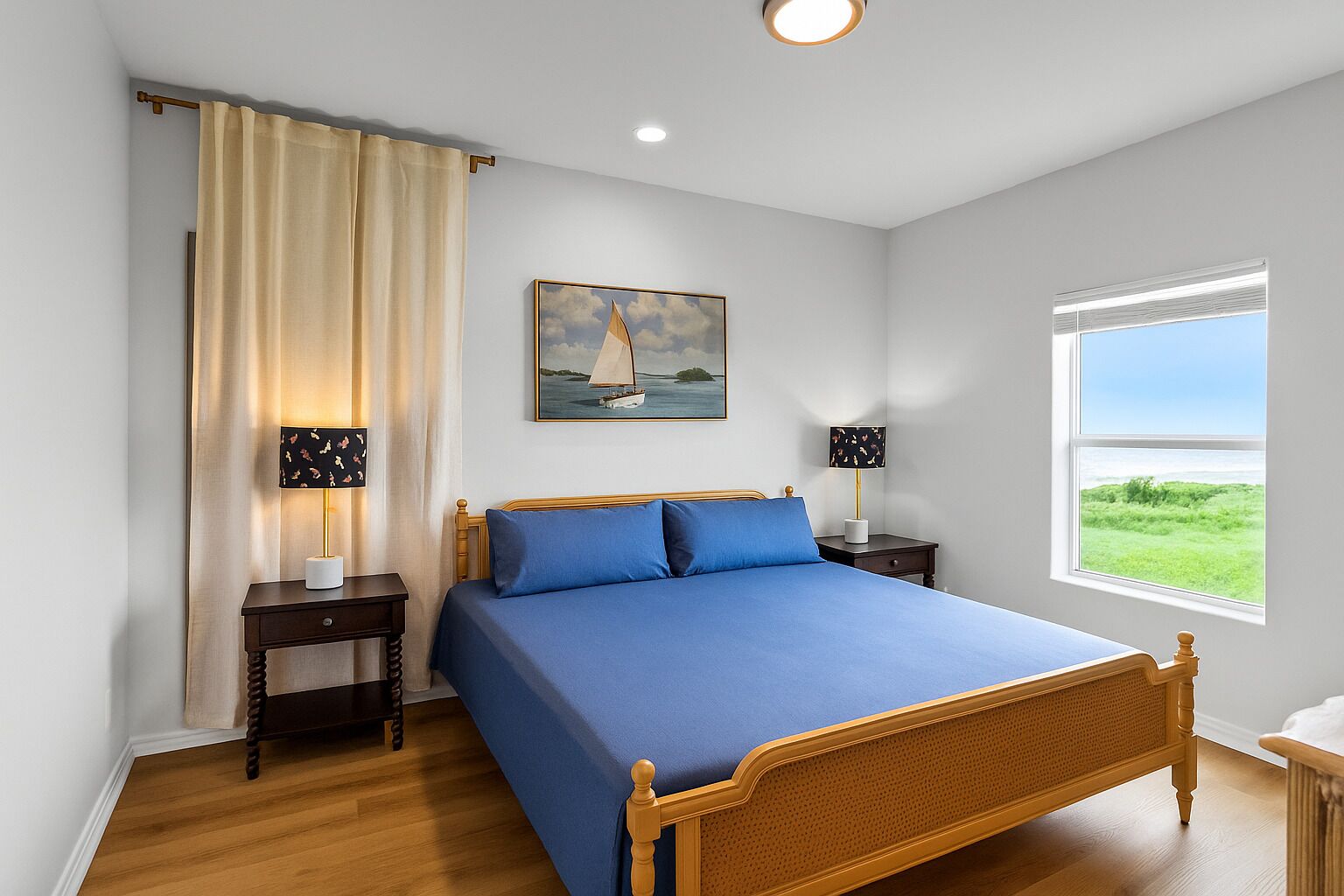 A bedroom with a bed, two bedside tables, a window with a view, a painting on the wall, and a curtain.
