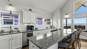 A modern kitchen with white cabinets, granite countertops, and a large island with bar stools. - Beachfront | Pool | Ocean Views, Loft & Bar (Gilchrist)
