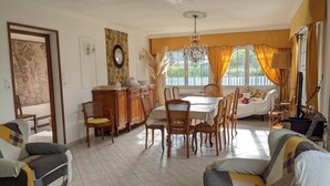 Een ruime woonkamer met een eethoek, met een kroonluchter, een bank en een televisie.