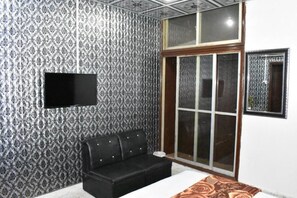 A room with patterned wallpaper, a black leather sofa, a flat-screen TV mounted on the wall, and a large window with a view. - Davis Hotel (Lahore)