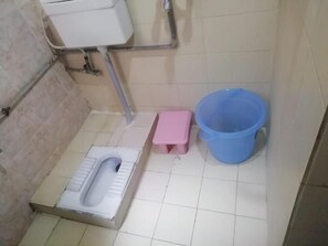 A small bathroom with a toilet, a pink stool, and a blue bucket. - Davis Hotel (Lahore)
