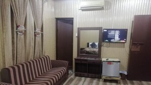 A living room with a striped sofa, a small TV, and a wooden cabinet. - Davis Hotel (Lahore)