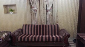A living room with a striped sofa, a small shelf with a plant, and curtains. - Davis Hotel (Lahore)