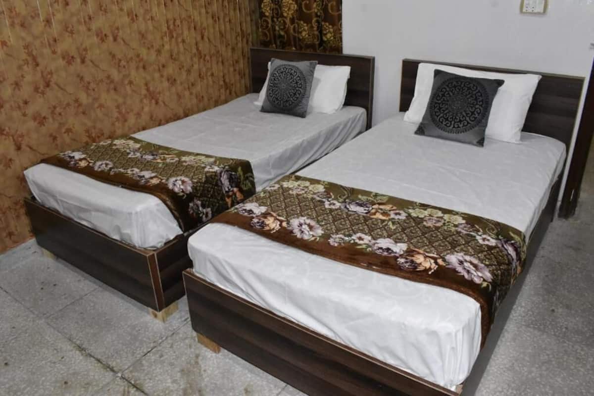 Two single beds with floral-patterned bedspreads and dark wooden headboards in a room with patterned wallpaper.