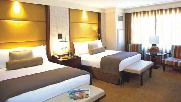 A hotel room with two beds, a small table with a magazine, a chair, and a lamp. - Davis Hotel (Lahore)
