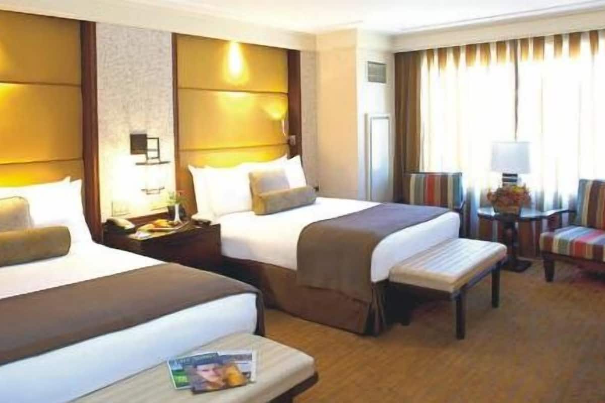 A hotel room with two beds, a small table with a magazine, a chair, and a lamp.