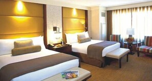 A hotel room with two beds, a small table with a magazine, a chair, and a lamp. - Davis Hotel (Lahore)