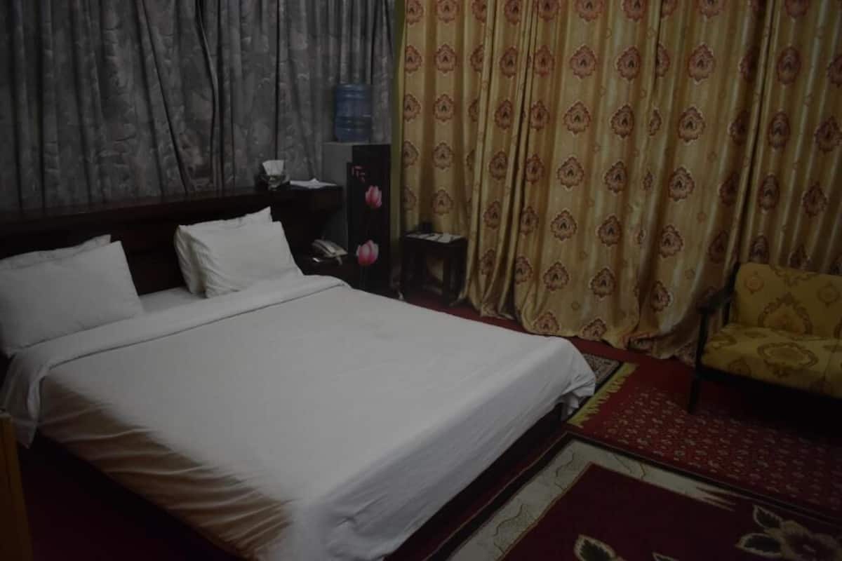 Un dormitorio con cama, mesita de noche, silla y cortinas.