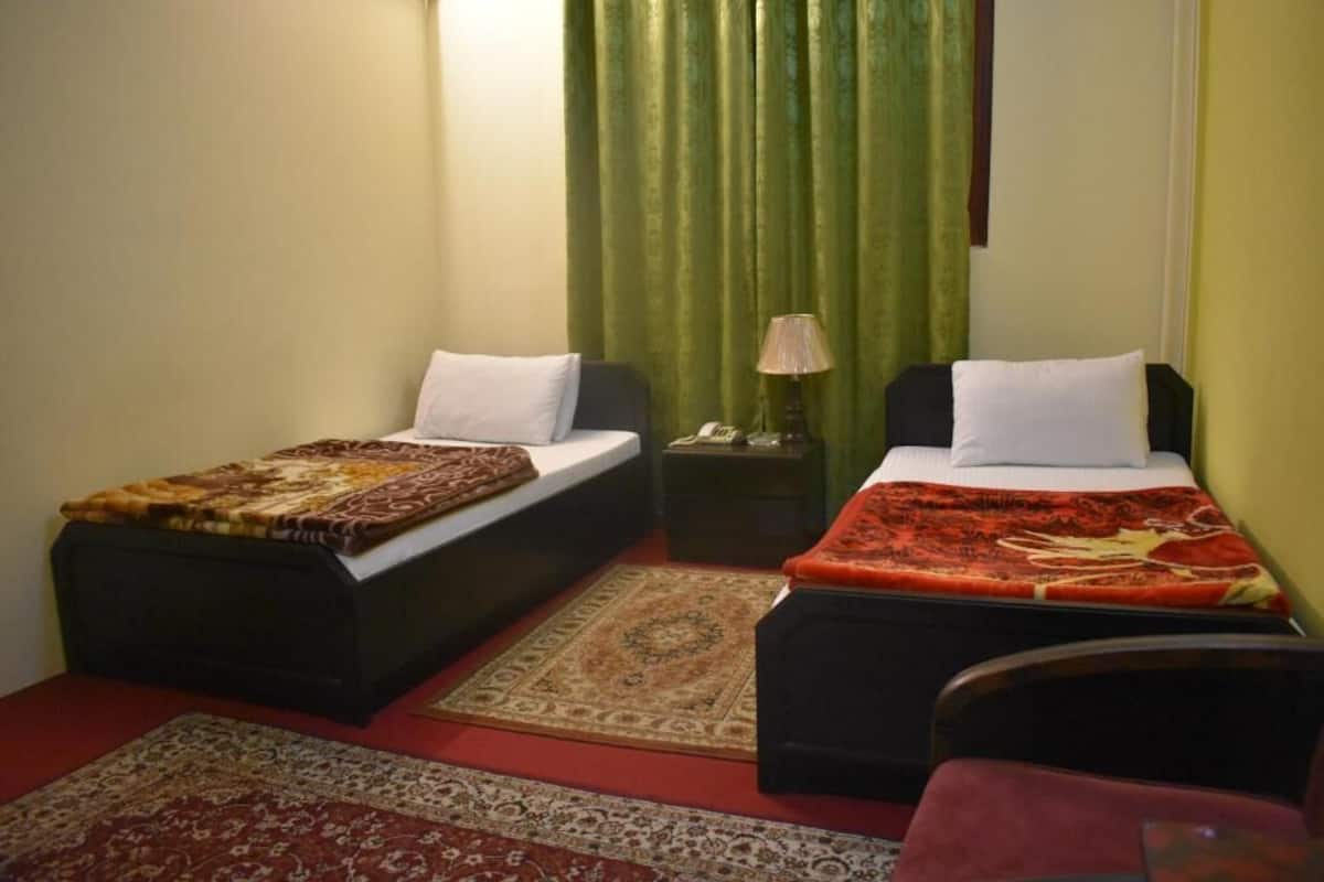 Una habitación pequeña con dos camas individuales, una mesita de noche con lámpara y una silla.
