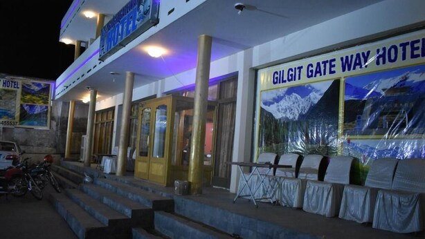 A hotel entrance with steps leading up to a covered area, a sign for Gilgit Gate Way Hotel, and a view of the mountains in the background. - Gilgit Gateway Hotel (Gilgit)