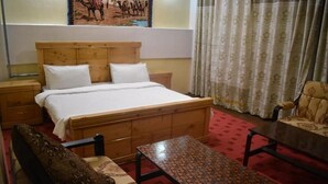 A hotel room with a wooden bed, a nightstand, a patterned sofa, a small table, and a patterned armchair. - Gilgit Gateway Hotel (Gilgit)