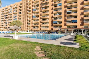A hotel with a swimming pool, lounge chairs, and a large building with balconies.