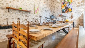Un espace repas avec une longue table en bois, dressée pour quatre personnes, entourée de chaises en bois dotées d’assises rembourrées.