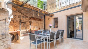 Un espace extérieur aménagé pour les repas, avec un mur en pierre, une pergola et une vue sur la rue.