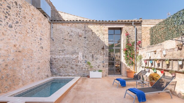 Une cour bordée de murs en pierre, avec une piscine, des chaises longues et des plantes en pot.