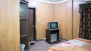 A bedroom with a bed, a television on a stand, a wardrobe, and a door. - Gardenia Hotel (Lahore)