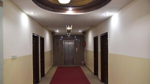 A hallway with a red carpet, two doors on each side, and an elevator at the end. - Gardenia Hotel (Lahore)