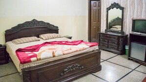 A bedroom with a wooden bed, a dresser, a television, and a mirror. - Gardenia Hotel (Lahore)
