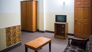 A room with a wooden cabinet, a television on a wooden stand, a wooden table, and a patterned sofa. - Gardenia Hotel (Lahore)