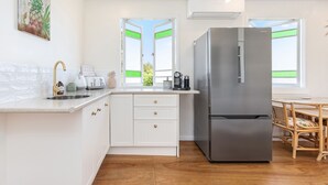 A modern kitchen with white cabinetry, a stainless steel refrigerator, a sink, and a dining area with a wooden table and chairs. - Villa Sunshine - Pet Friendly Fully Air conditioned (Toogoom)