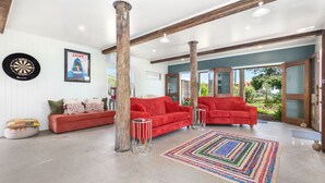 A spacious living room with a red sofa, a colorful rug, and a dartboard. - Villa Sunshine - Pet Friendly Fully Air conditioned (Toogoom)