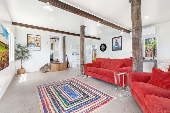 A spacious living room with a red sofa, a colorful rug, and a wooden ceiling beam. - Villa Sunshine - Pet Friendly Fully Air conditioned (Toogoom)