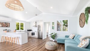 A modern kitchen with white cabinetry, a central island with stools, and a dining area with a light blue sofa and ottoman. - Villa Sunshine - Pet Friendly Fully Air conditioned (Toogoom)