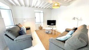 A modern living room with two grey sofas, a flat-screen TV, a wicker lamp, and a white ceiling with exposed beams.