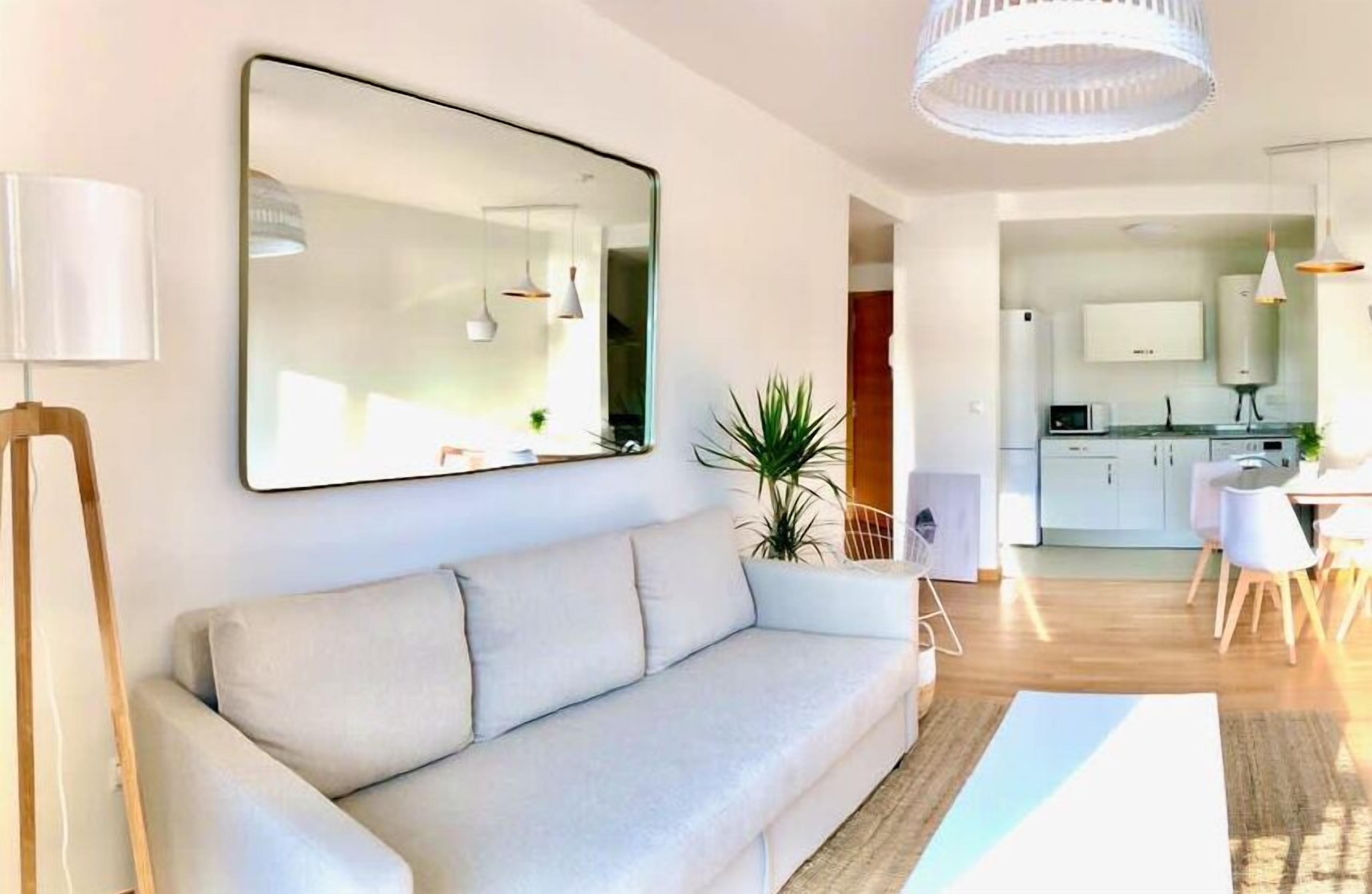 Un salon moderne avec un canapé, un grand miroir et un coin repas comprenant une table et des chaises.