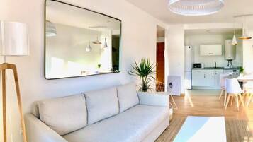 Un salon moderne avec un canapé, un grand miroir et un coin repas comprenant une table et des chaises.