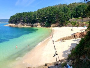 A beach with clear turquoise water, a sandy shore, and a forested hill in the background.
