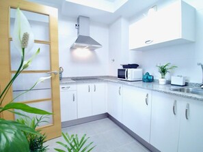 A modern kitchen with white cabinets, a stainless steel range hood, a microwave, and a sink. - The Cliffs - Sunset Village Beach 3E (Viveiro)