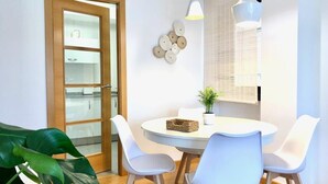 A dining area with a round table, white chairs, a potted plant, and a wooden door with glass panels. - The Cliffs - Sunset Village Beach 3E (Viveiro)