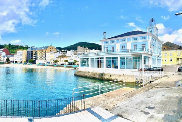 Un bâtiment situé au bord de l’eau, doté d’un balcon, d’une tour horloge et offrant une vue dégagée sur l’eau.