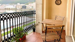 A balcony with a wooden table and chairs, a potted plant, and a view of a cityscape and mountains. - The Cliffs - Marina Sol te hará soñar (Viveiro)